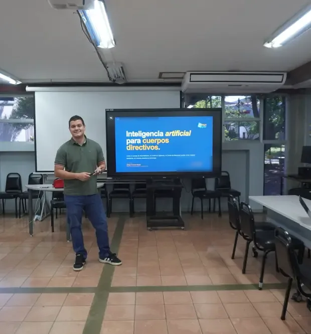 Diego Cordero junto a una pantalla con la presentación de inteligencia artificial para cuerpos directivos, en una sala de capacitación